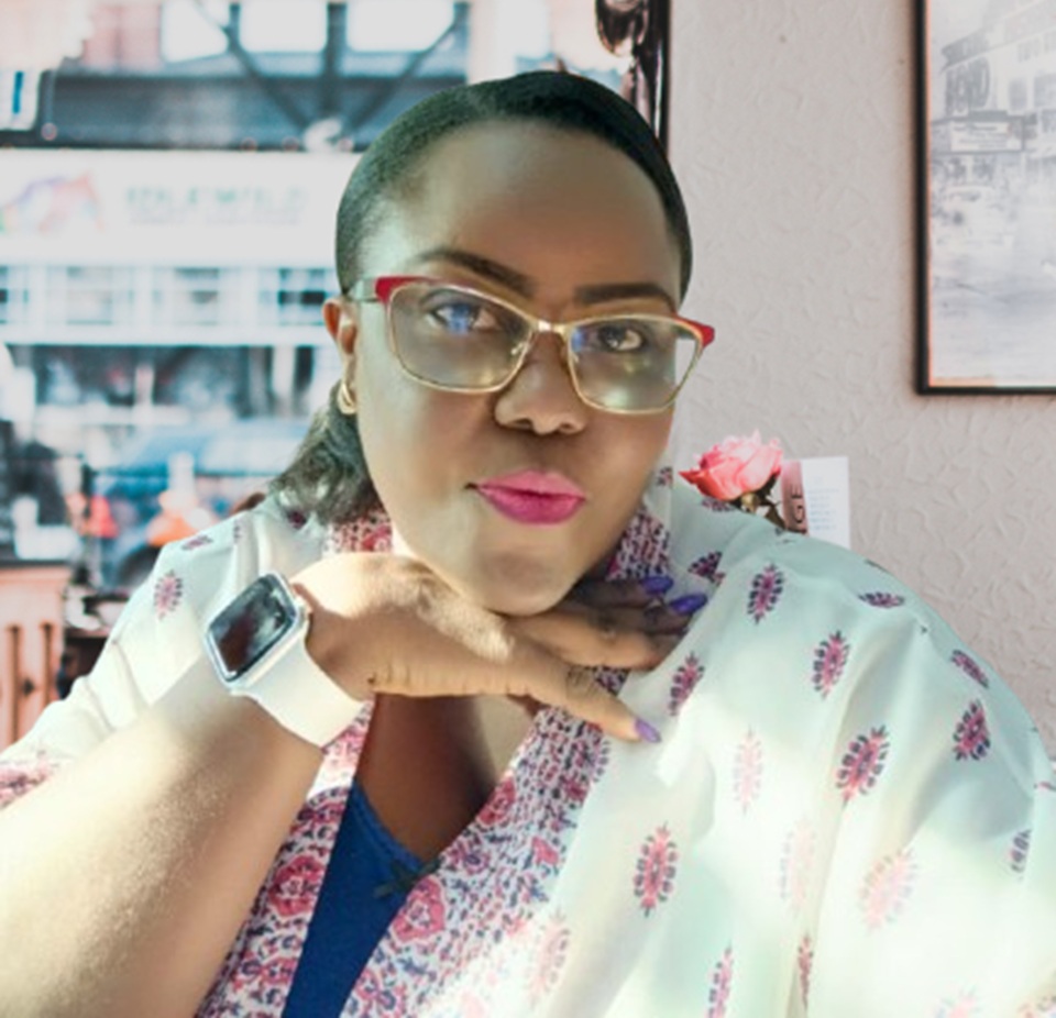 A woman with glasses and a floral shawl poses confidently with a playful gesture, set against a blurred background of a lively street scene.